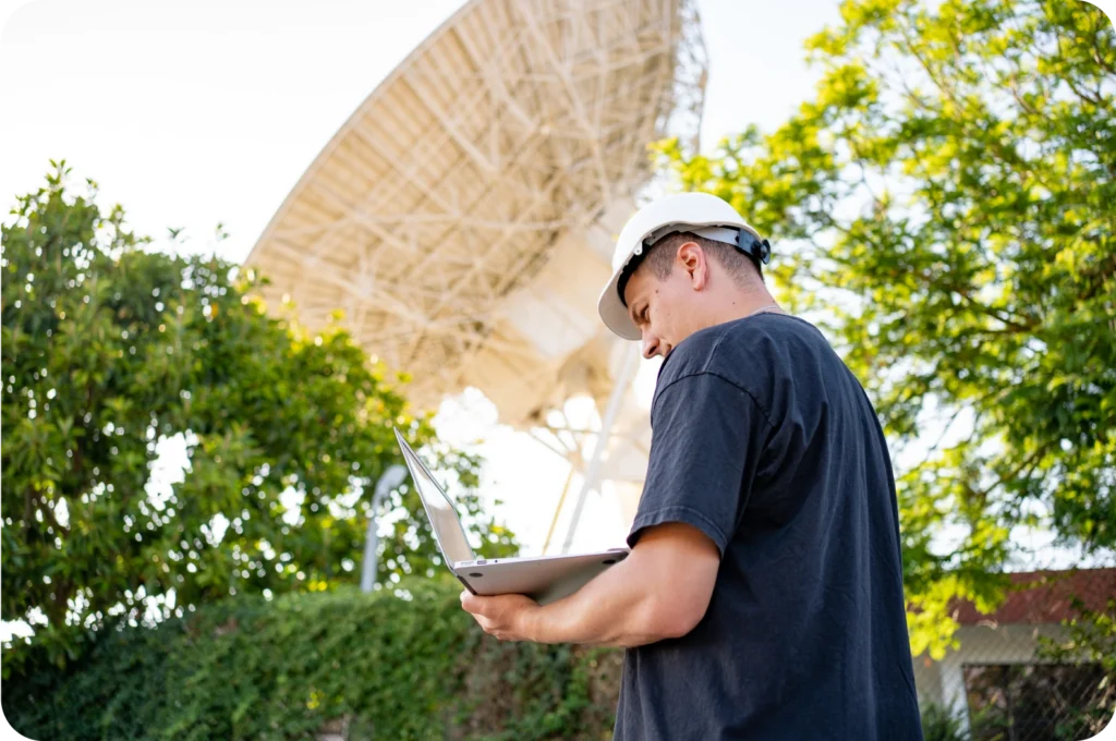 Worker using laptop near large satellite dish