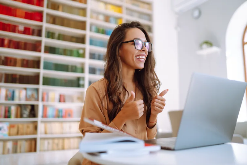 Smiling woman giving thumbs up at laptop.
